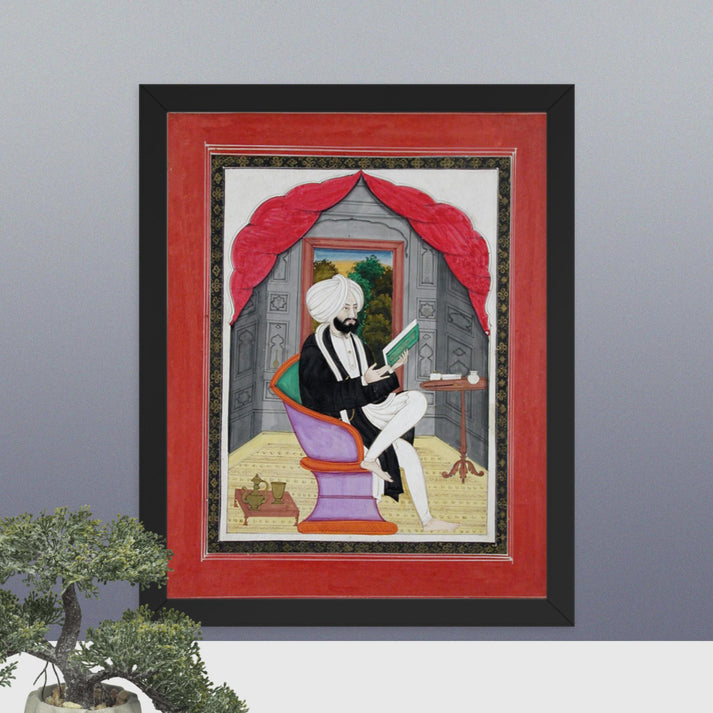 A Sikh Sardar reading from a book, seated in front of a window - Framed Print