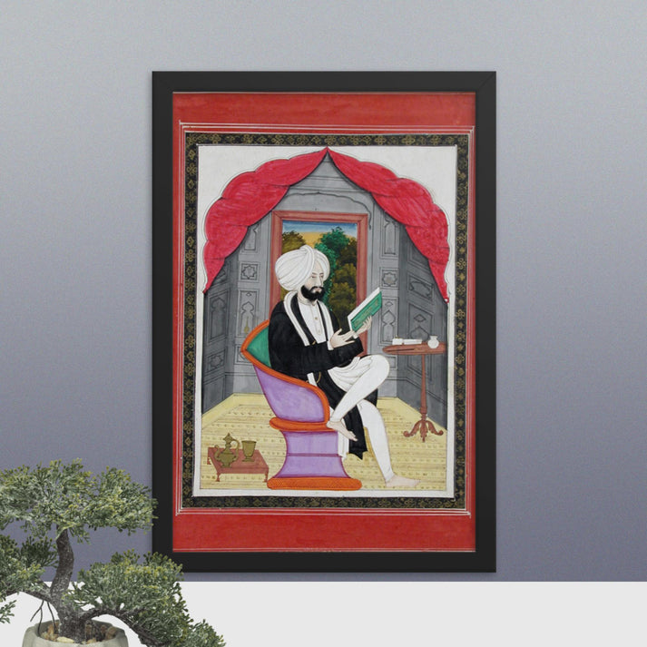 A Sikh Sardar reading from a book, seated in front of a window - Framed Print