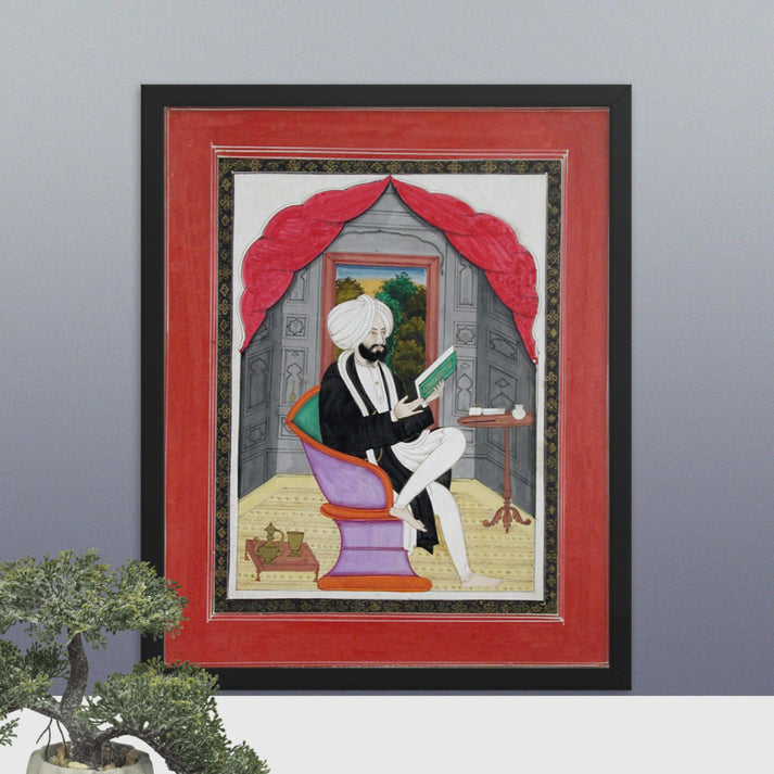 A Sikh Sardar reading from a book, seated in front of a window - Framed Print